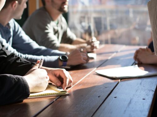 people sitting on chair in front of table while holding pens during daytime