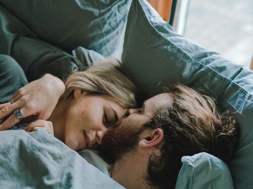 man kissing woman's forehead while lying on bed