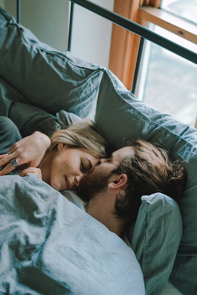 man kissing woman's forehead while lying on bed