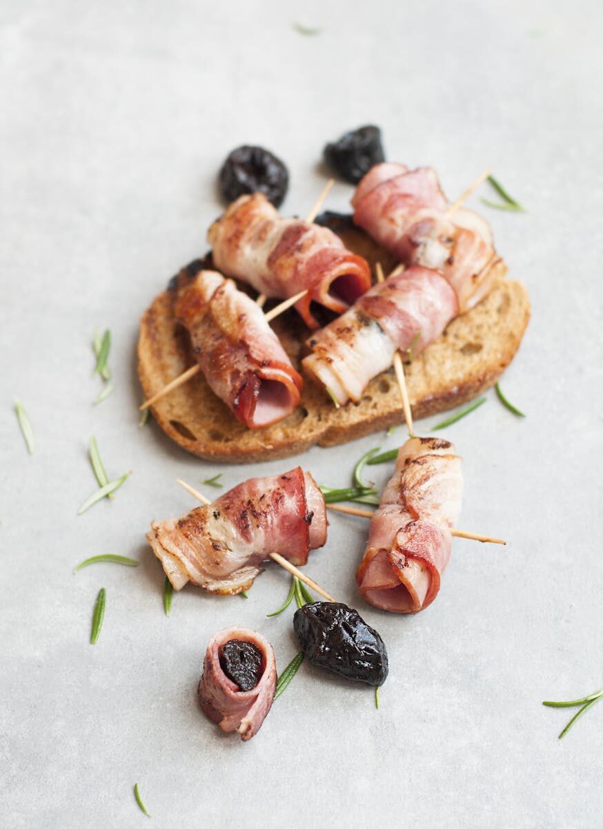 Delicious bacon-wrapped prunes with rosemary on rustic bread. Perfect appetizer idea.