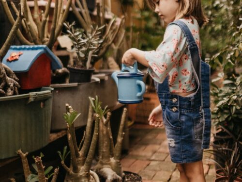 girl wearing blue romper holding teal watering can