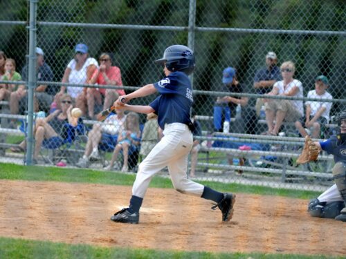 boy batting baseball near catcher beside gray fence