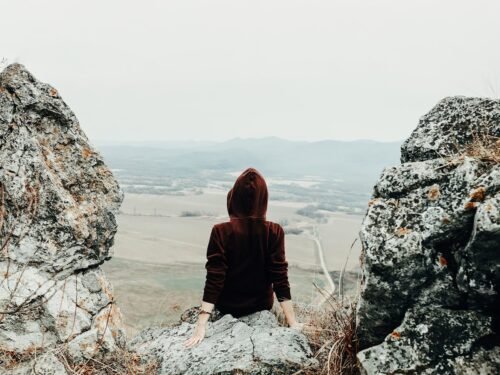 woman in brown hoodie sitting on rock formation during daytime