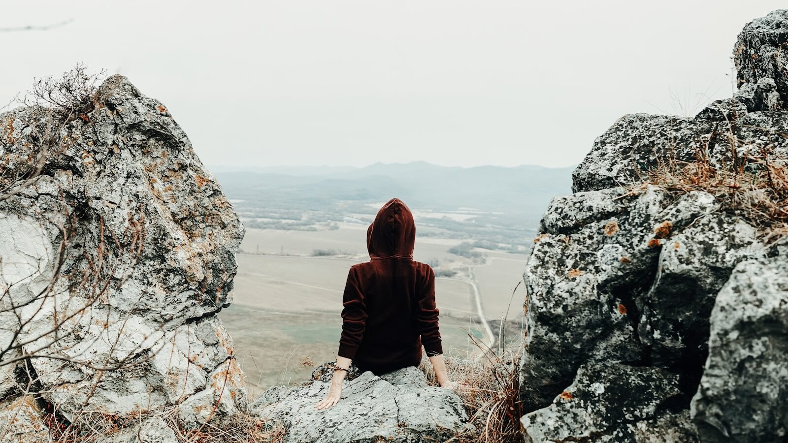 woman in brown hoodie sitting on rock formation during daytime