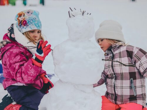 two girl molding a snowman during daytime