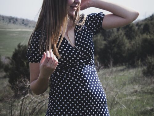 woman in black and white polka dot dress standing on green grass field during daytime