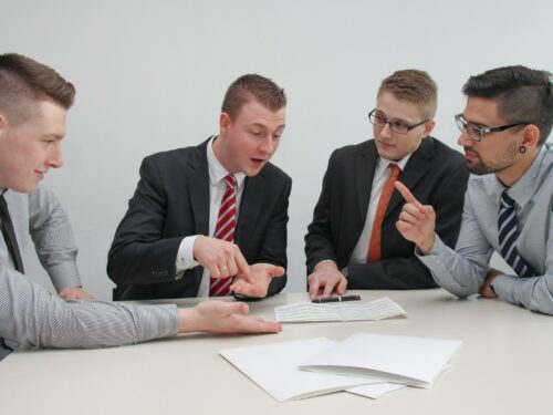 four men sitting at desk talking