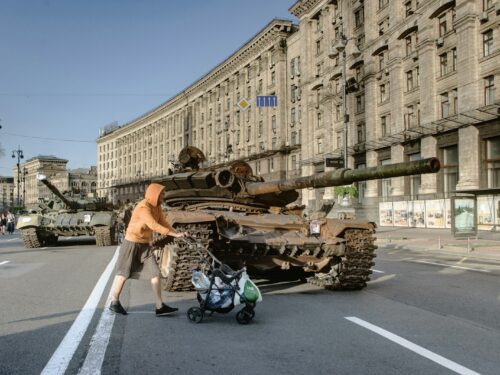 a man pushing a stroller past a tank on the street