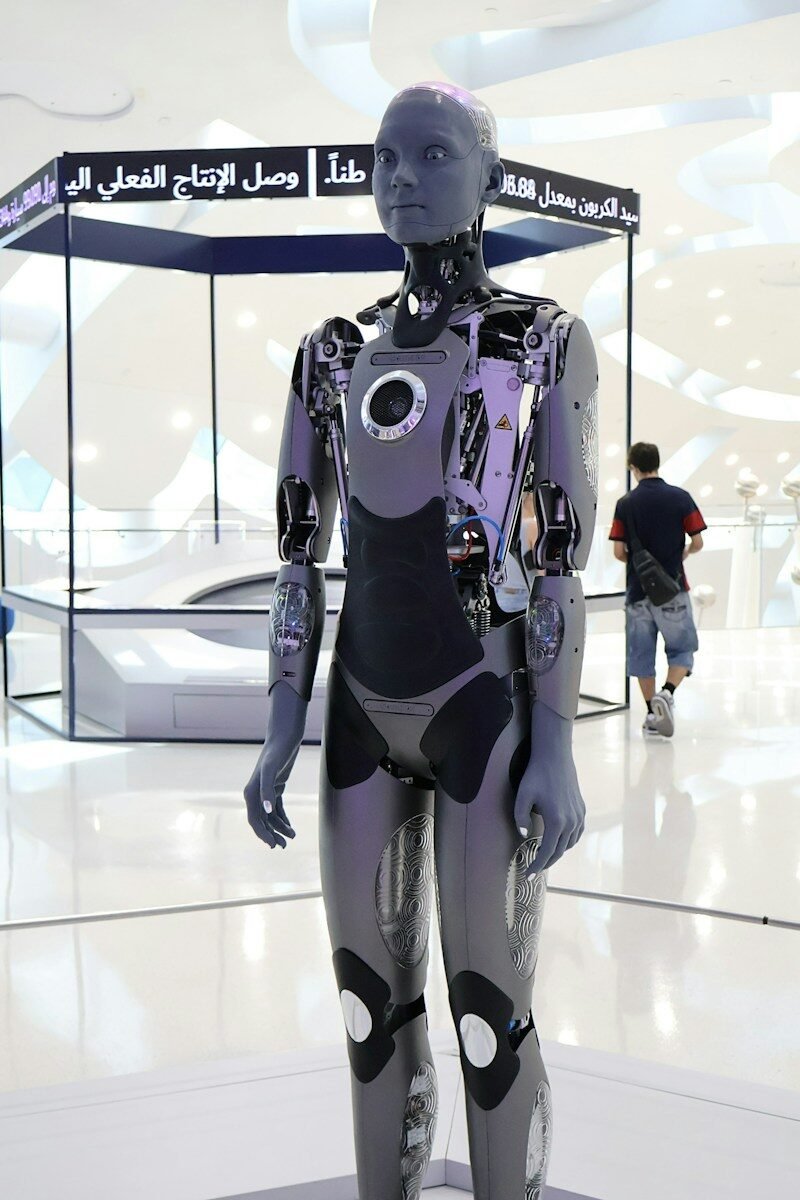 A grey humanoid robot with exposed mechanical joints in a bright exhibition hall