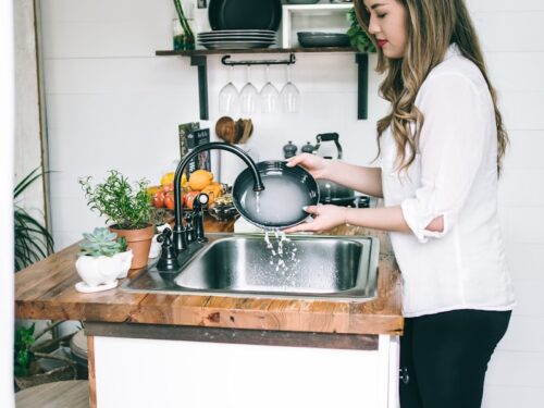 woman wearing white blouse washing dish on the faucet