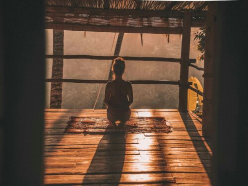 woman meditating on floor with overlooking view of trees