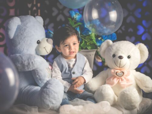 boy in blue dress shirt sitting beside white bear plush toy