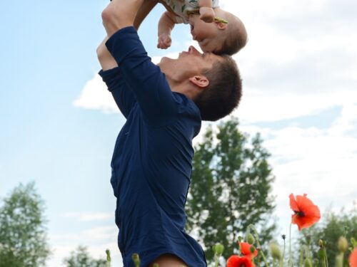 man in blue long sleeve shirt carrying baby in white onesie