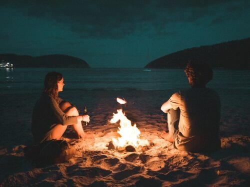 man and woman with bone fire sitting on seashore