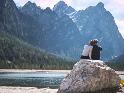 a couple sits on a rock looking out over a lake