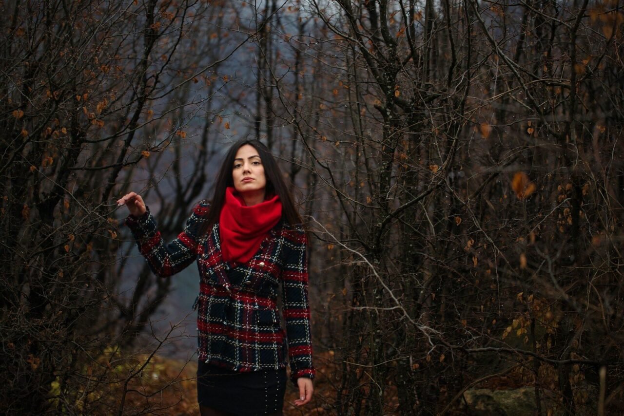 a woman in a red scarf is standing in the woods