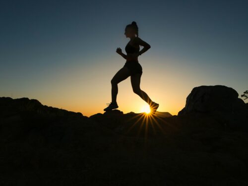 silhouette of man jumping on rocky mountain during sunset