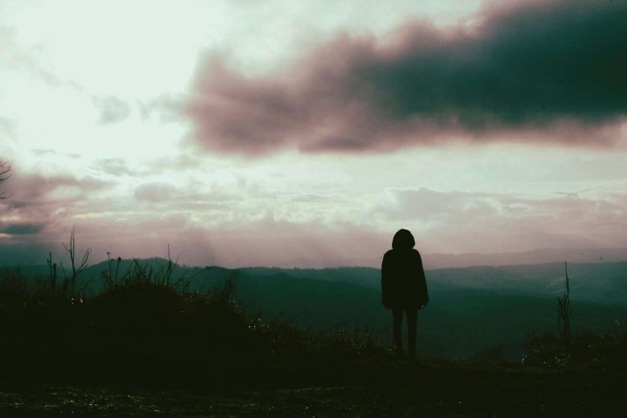 a person standing on top of a hill under a cloudy sky