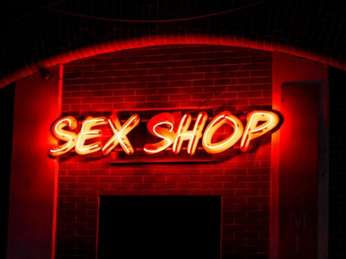 a neon sign that reads sex shop on a brick wall