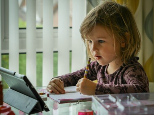 girl in purple and black long sleeve shirt holding black pen writing on white paper