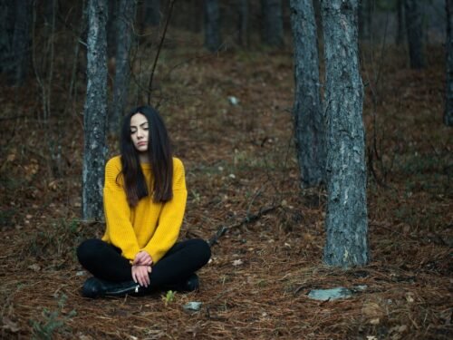 a woman in a yellow sweater is sitting in the woods