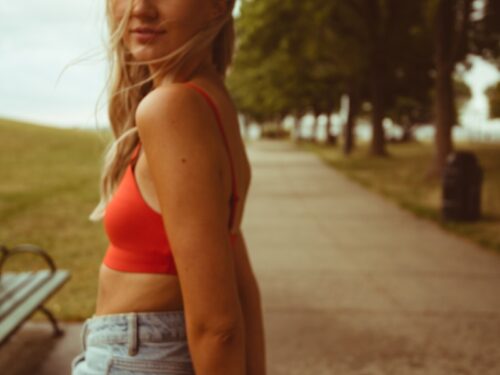 woman in red sports bra and blue denim shorts standing on gray concrete road during daytime