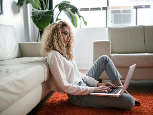 woman sitting on floor and leaning on couch using laptop