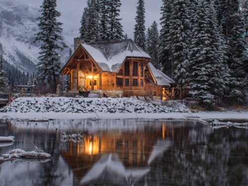 wooden house near pine trees and pond coated with snow during daytime