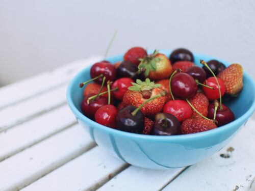 focus photography of strawberries and cherries on blue bowl