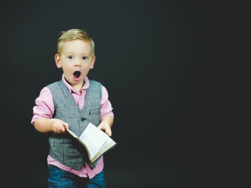 boy wearing gray vest and pink dress shirt holding book