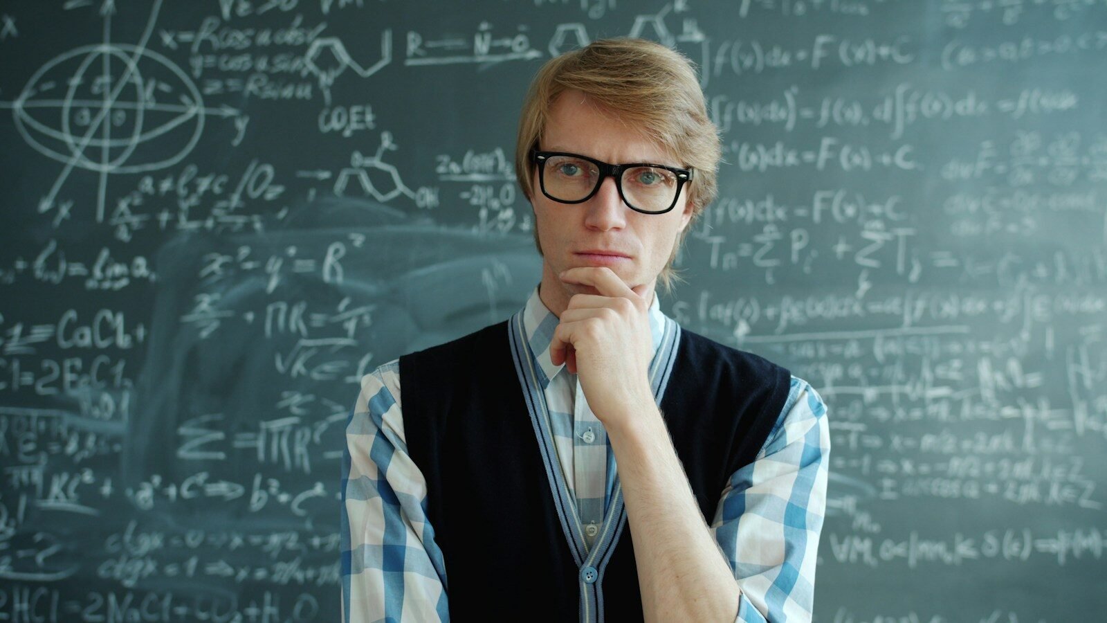 Man with glasses thinks in front of chalkboard
