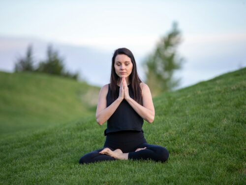 woman in black tank top and black pants sitting on green grass field during daytime