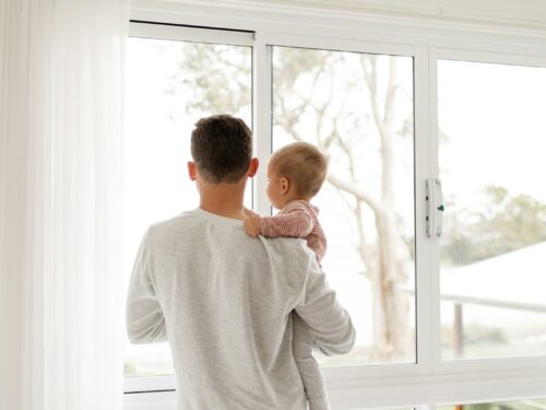 boy in gray sweater standing beside window during daytime