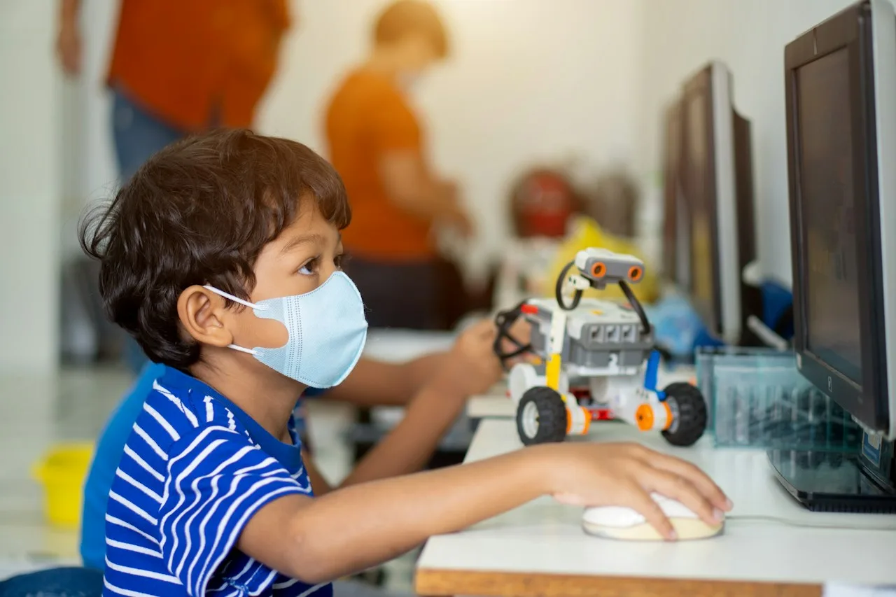 a young boy wearing a face mask while playing with a computer