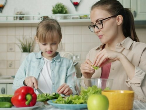 Mother and daughter preparing salad in kitchen.