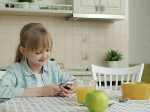 Girl using smartphone at kitchen table with breakfast