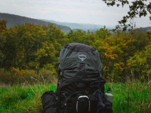 A large backpack sits on grassy ground with hills behind.