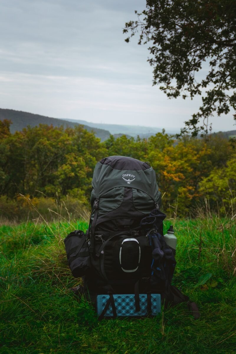 A large backpack sits on grassy ground with hills behind.