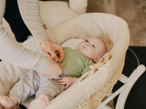 baby in green onesie lying on white crib