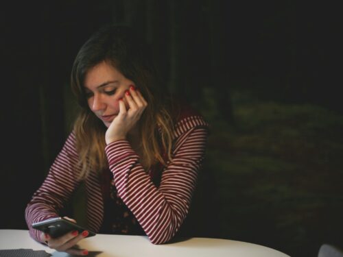 woman leaning on white wooden table while holding black Android smartphone