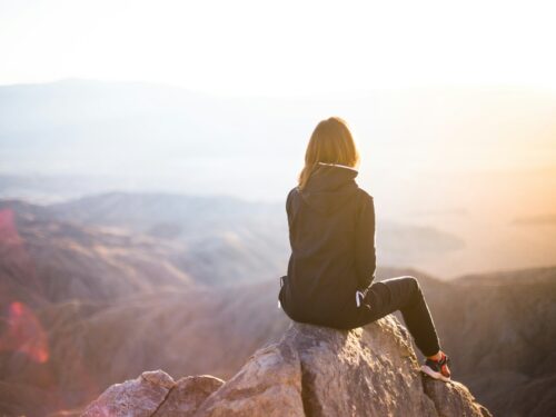 person sitting on top of gray rock overlooking mountain during daytime