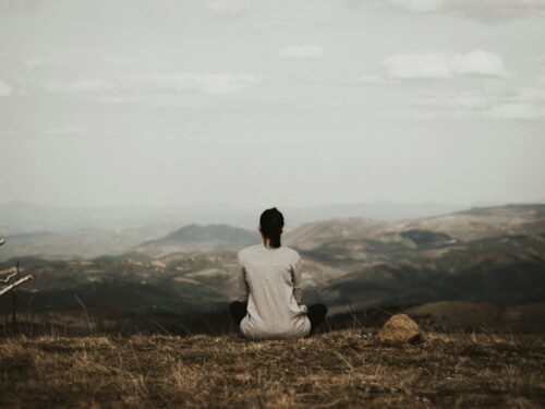 woman sitting on cliff overlooking mountains during daytime